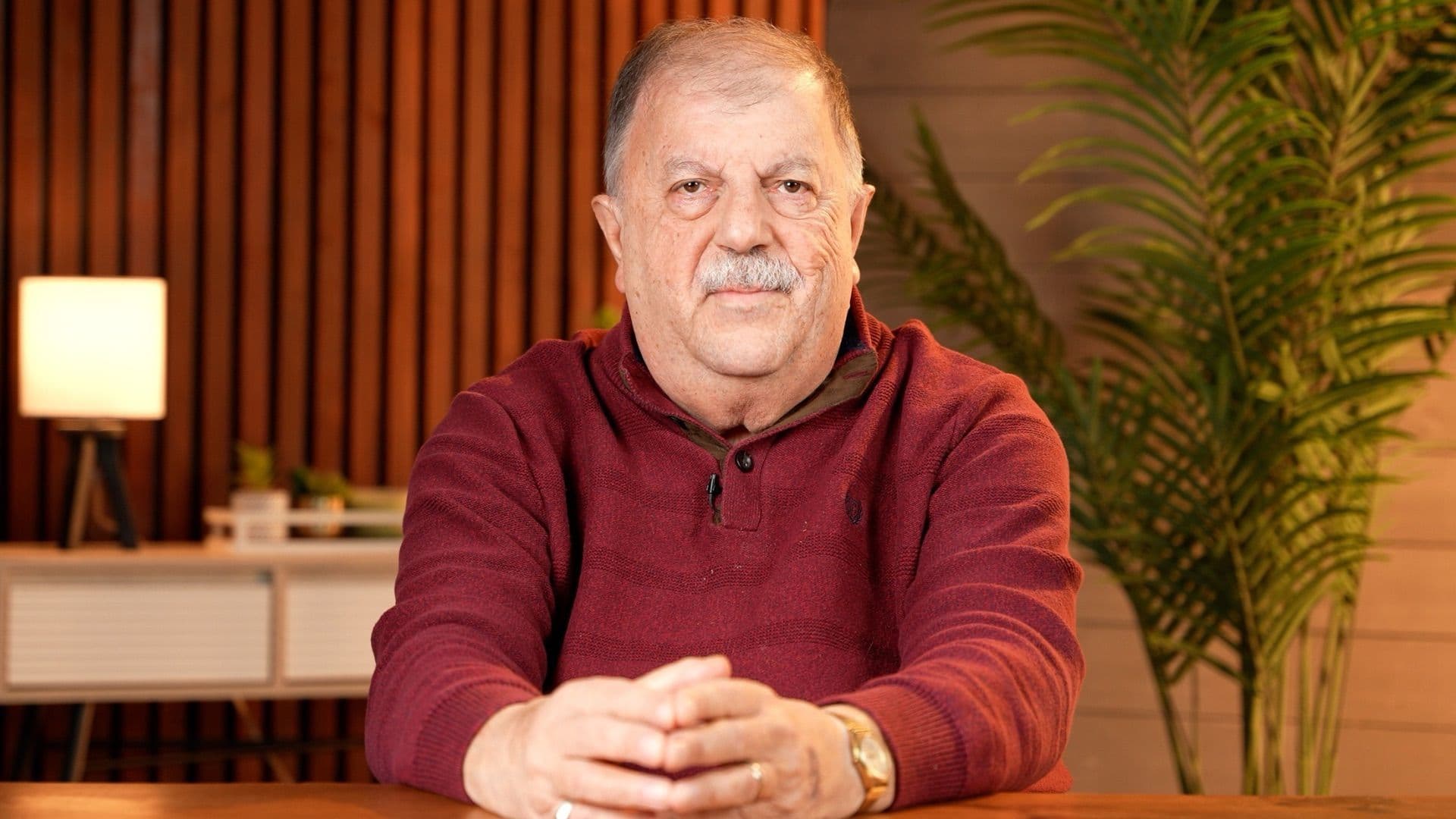 Portrait of Rev. John Franich seated at a table in a warm studio setting
