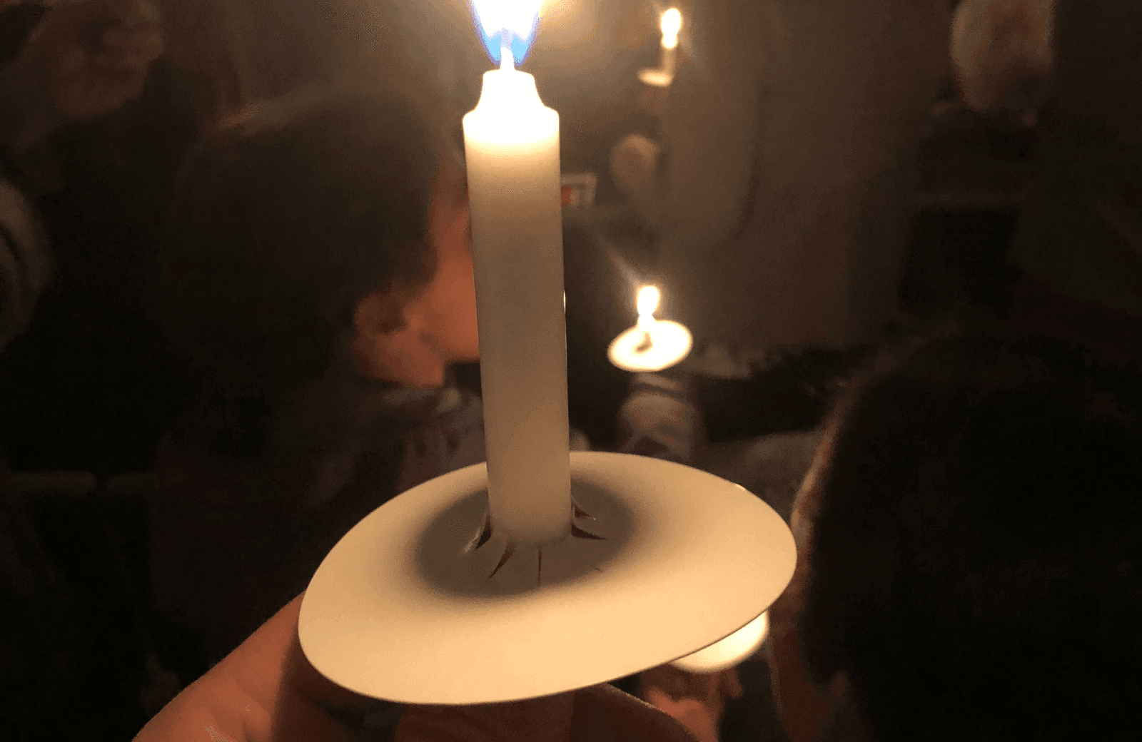 Hand holding a lit candle during Christmas Eve service with other candles glowing softly in background