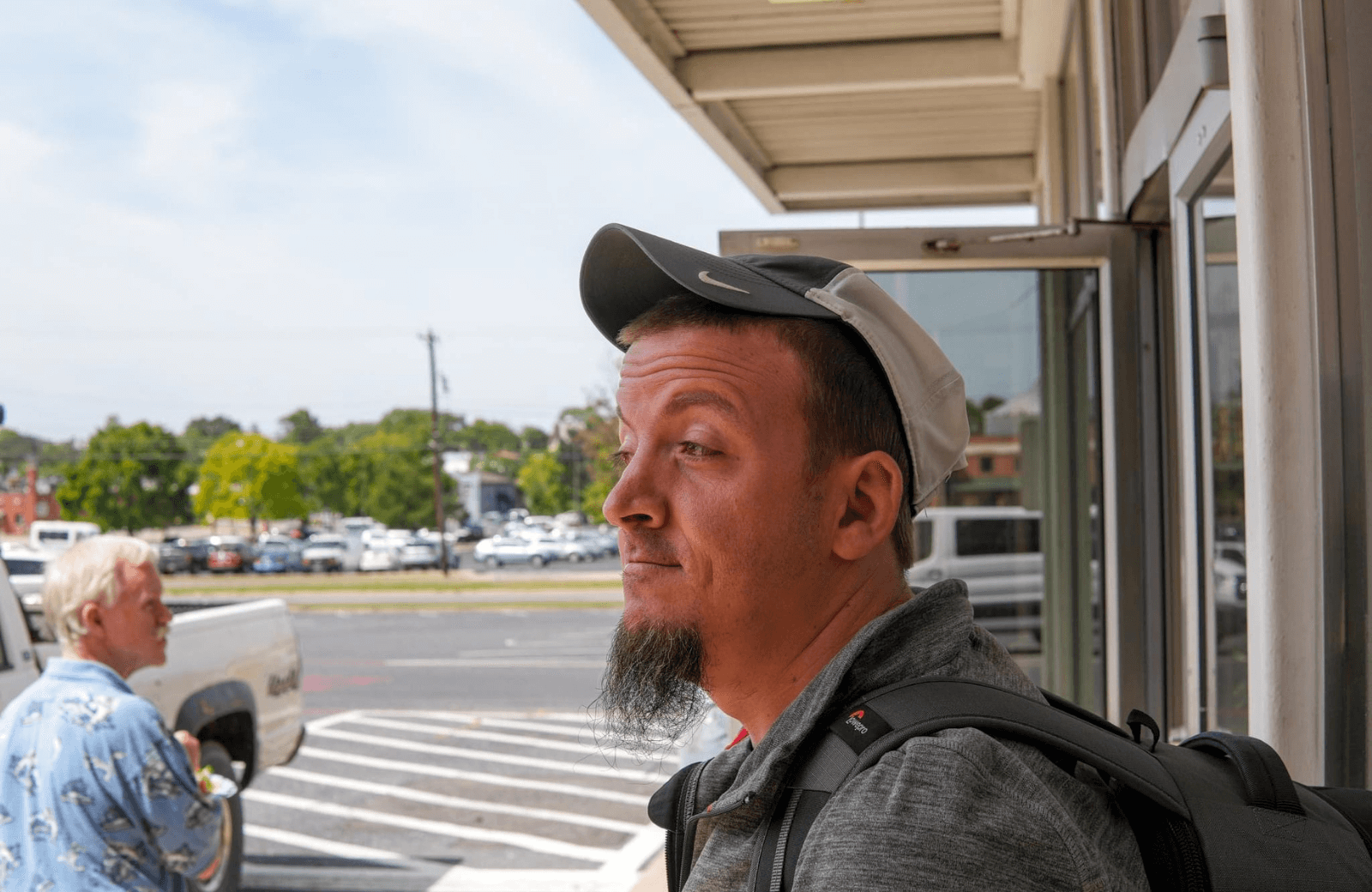 Man with backpack standing at a doorway, looking back over his shoulder at a parking lot