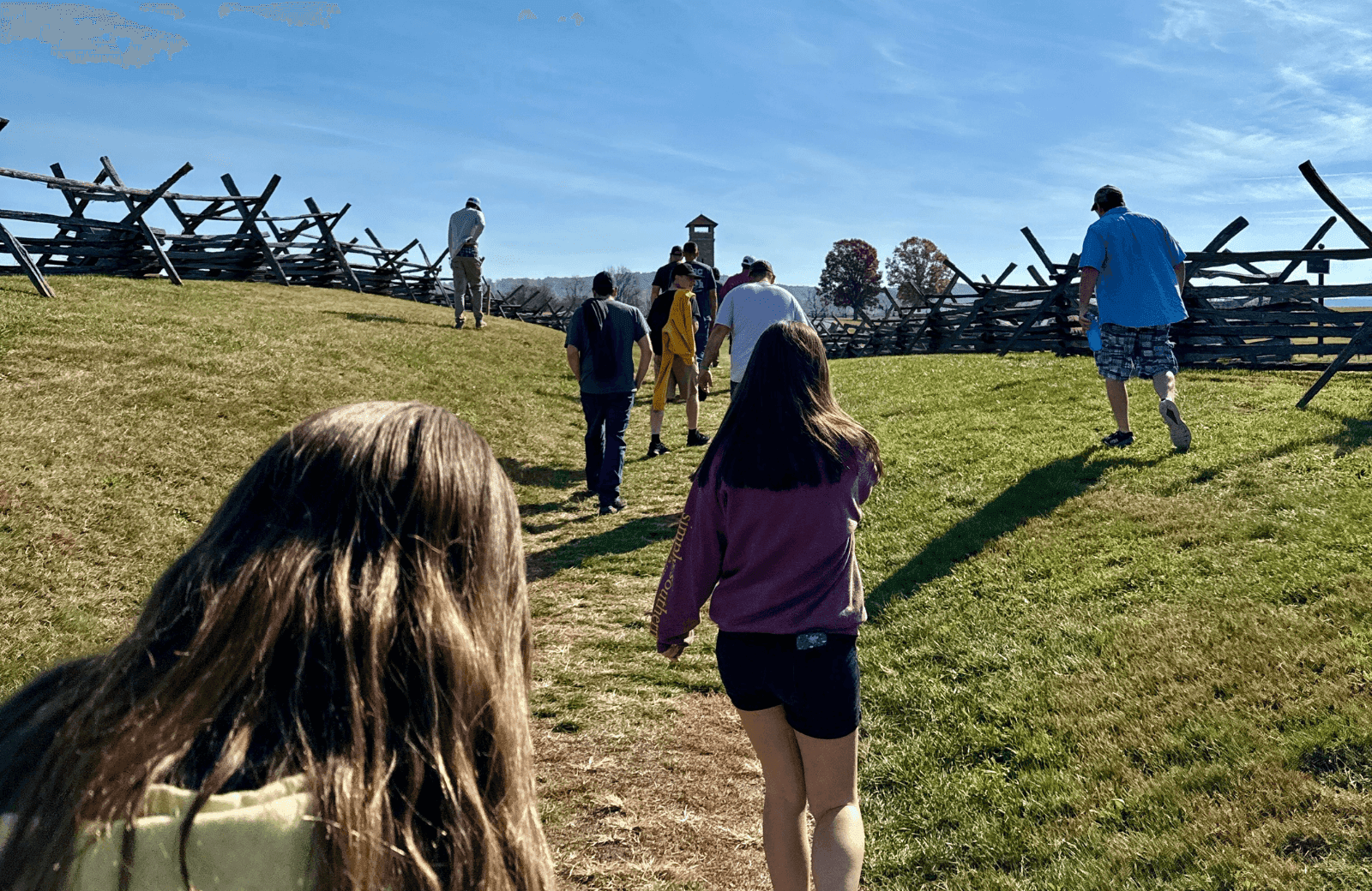 Two young girls walking on a grassy path at Antietam battlefield, following a group ahead on an autumn day
