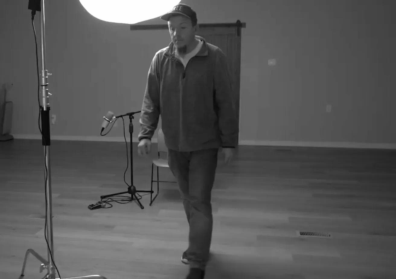 Justin Franich walking through the empty ministry building with a microphone and studio light in the background, black and white.